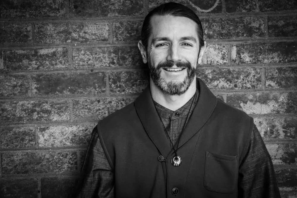 Black and white portrait of Patrick Mallan standing against a brick wall